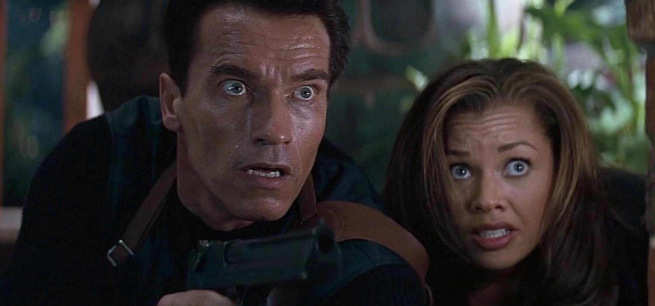 Arnold Schwarzenegger está sentado ao lado de Vanessa Williams e encara Eraser.