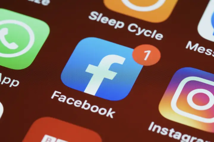 iPhone 主屏幕上的 Facebook 应用程序图标，周围有其他应用程序图标。