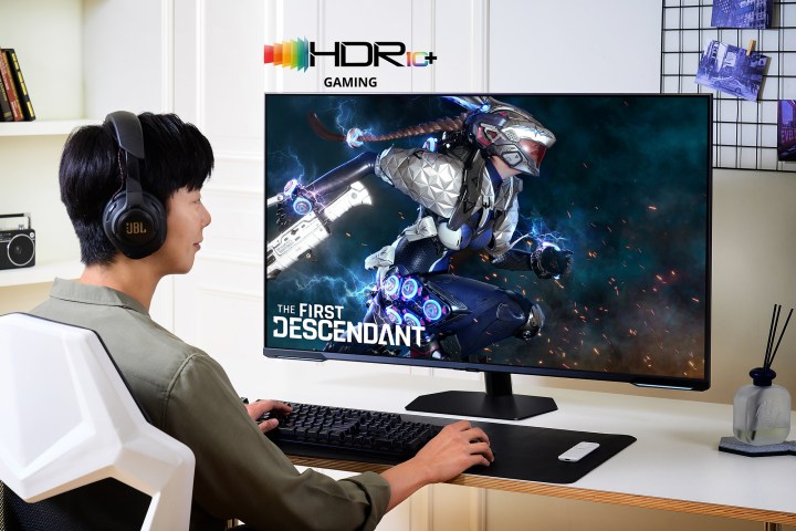 A man sits at a desk, playing The First Descendant. The man is using a Samsung Odyssey Neo G9 monitor.