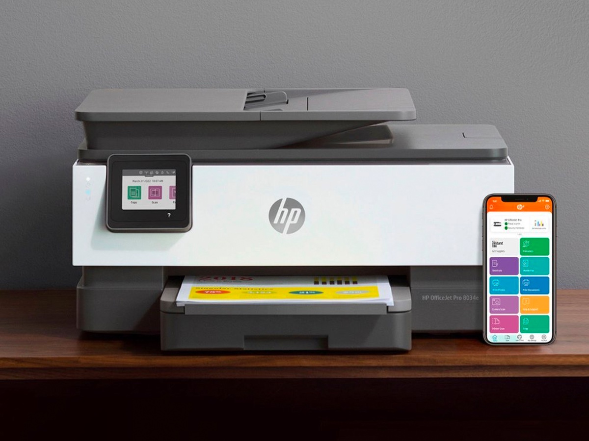 Impressora a jato de tinta multifuncional HP - OfficeJet Pro 8034e sem fio em uma mesa com um smartphone.