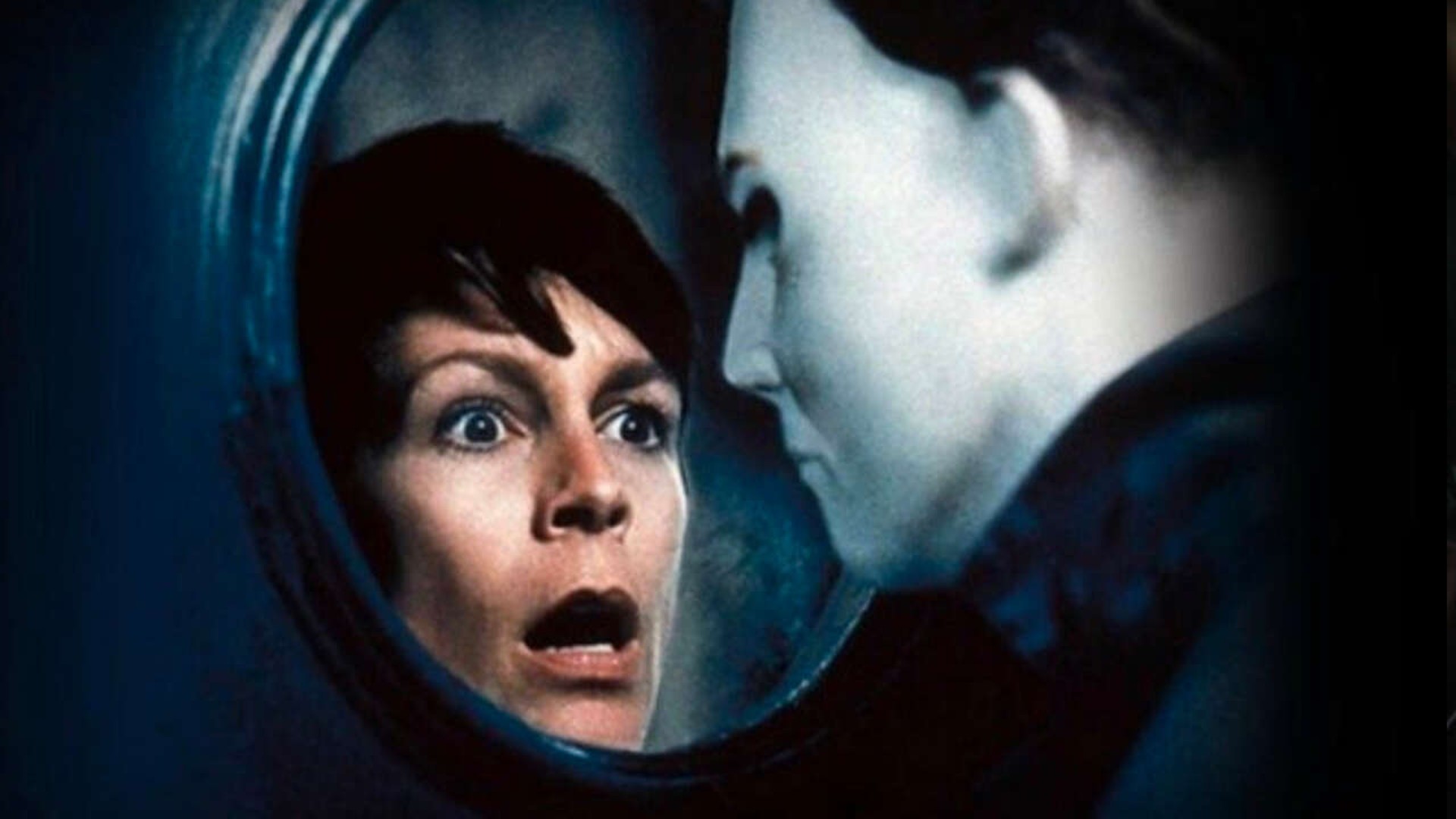 Jamie Lee Curtis stares with horror through a round window at the masked face of Michael Myers.