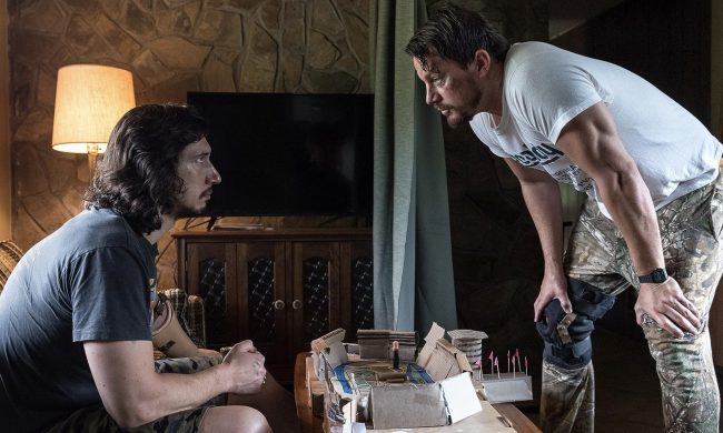 Adam Driver sits on the couch as Channing Tatum stands over him in Logan Lucky.