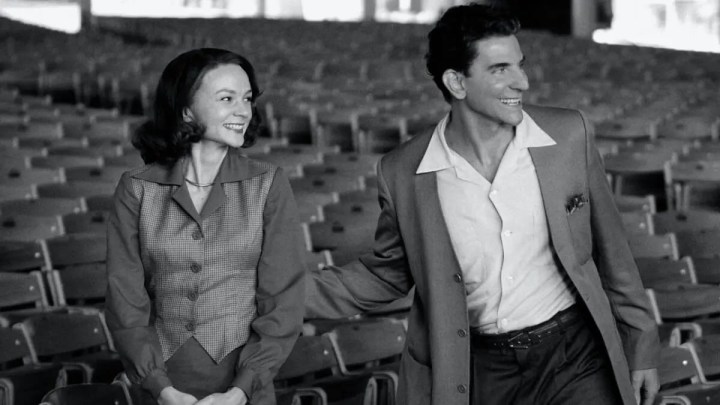 Carey Mulligan e Bradley Cooper como Felicia Montealegre e Leonard Bernstein sorrindo enquanto olham na mesma direção em Maestro.