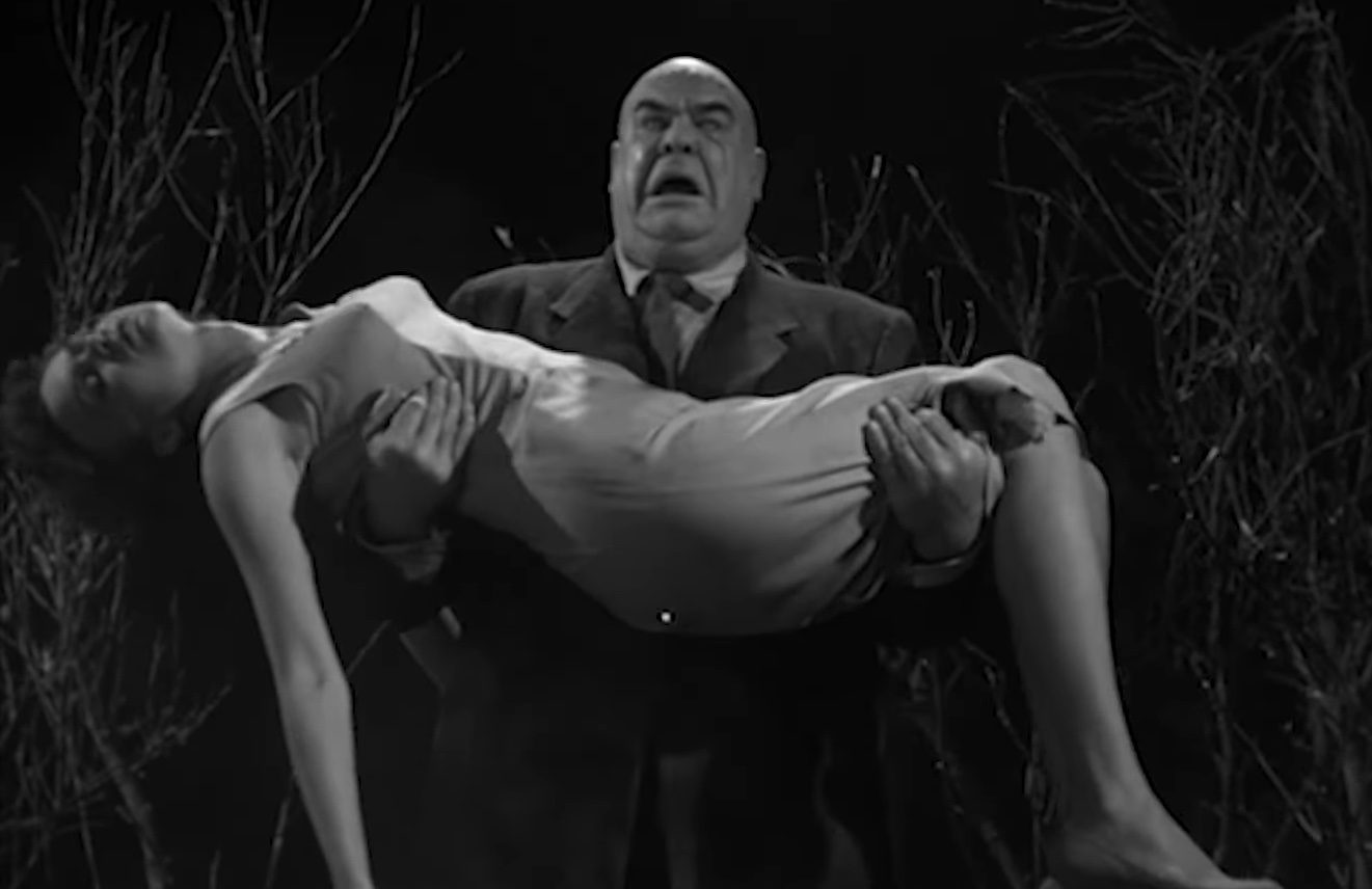"बाह्य अंतरिक्ष से योजना 9" में एक पुरुष एक महिला के शरीर को अपनी बाहों में पकड़े हुए है।