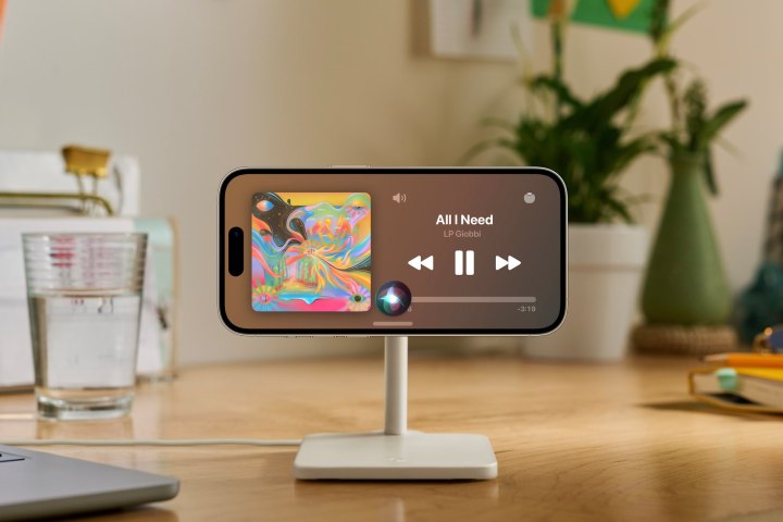 iPhone on charging stand showing now playing screen in iOS 17 StandBy mode.