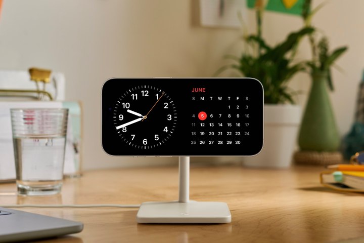 iPhone на подставке для зарядки с виджетами часов и календаря в режиме ожидания iOS 17.