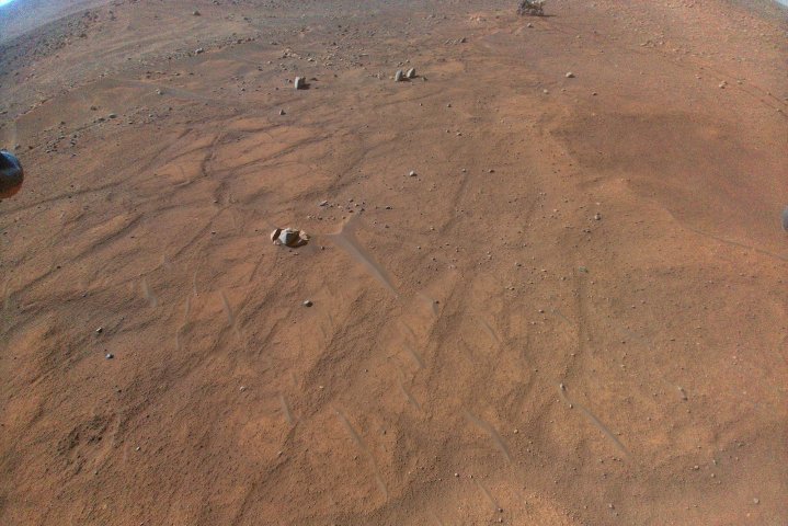 An aerial image of the Mars landscape captured by the Ingenuity helicopter, with the Perseverance rover also in the frame.