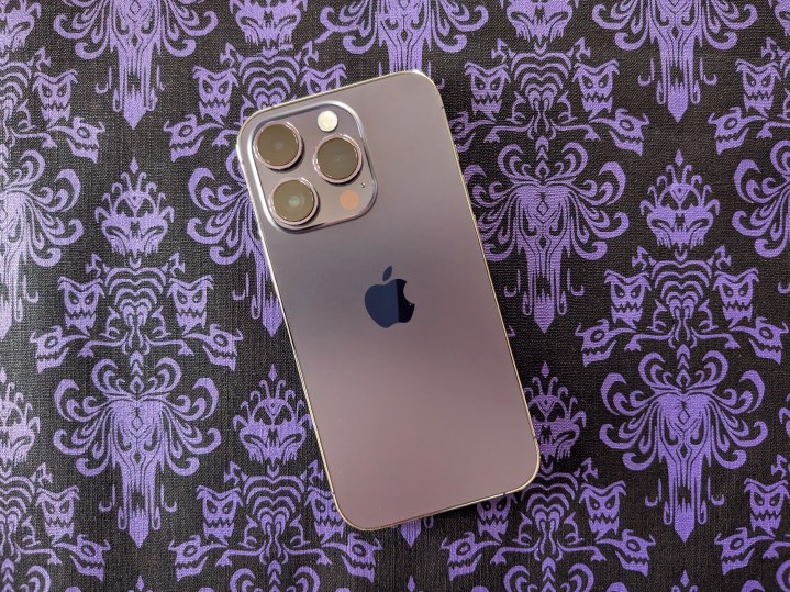 A Deep Purple iPhone 14 Pro on top of a Haunted Mansion wallpaper placemat.