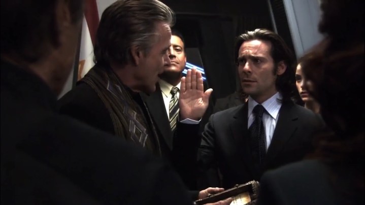 Gaius Baltar raises his hand as he is sworn in as President in the Battlestar Galactica episode "Lay Down Your Burdens, Part 2"