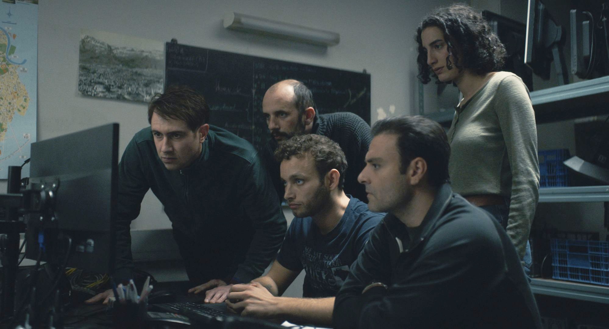 Um grupo de detetives olha para um computador em A noite do dia 12.