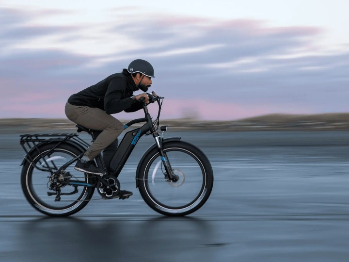 A male rider crouched down riding an Ariel eBikes Kepler fat tire e-bike on hard-packed beach sand.