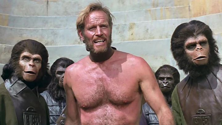 Charlton Heston como George Taylor de pie con un grupo de simios en El planeta de los simios de 1968.