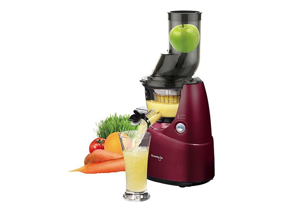 The Kuvings wide-mouth slow juicer and some fruits and vegetables against a white background.