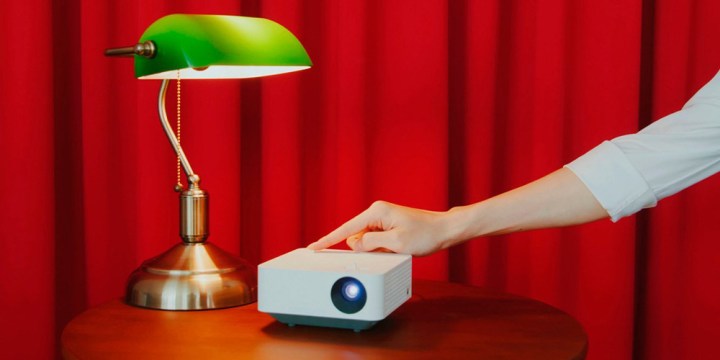 The LG CineBeam PF510Q Full HD 1080p smart projector on a cabinet next to a light.