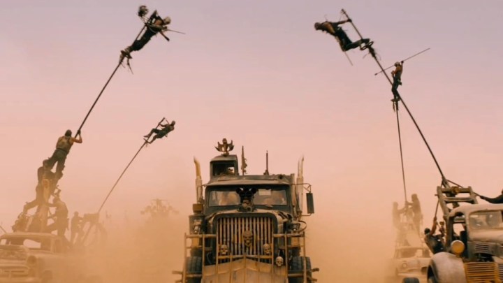 Los hombres se balancean desde postes mientras conducen autos en el desierto.