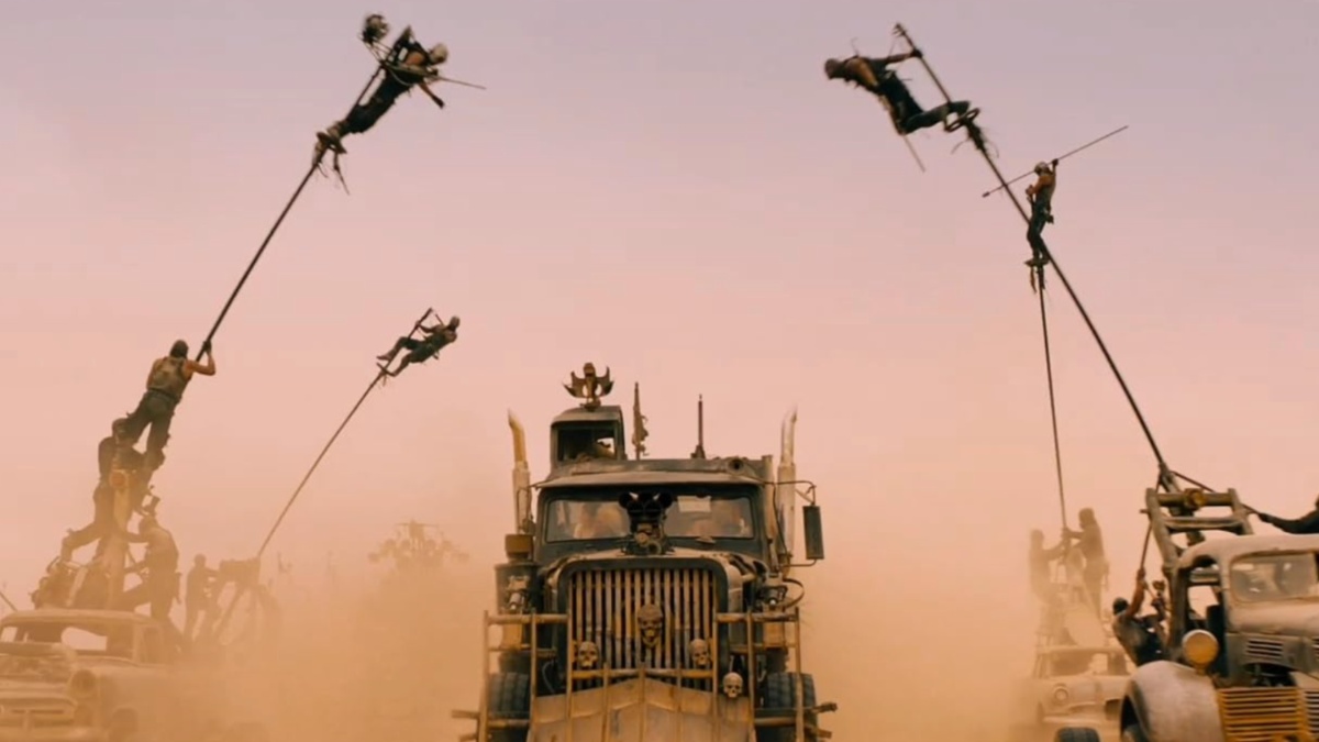 Los hombres se balancean desde postes mientras conducen autos en el desierto.