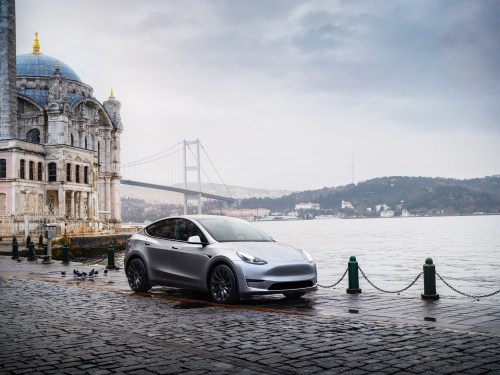 A Tesla 3 sits parked beside an urban waterfront.