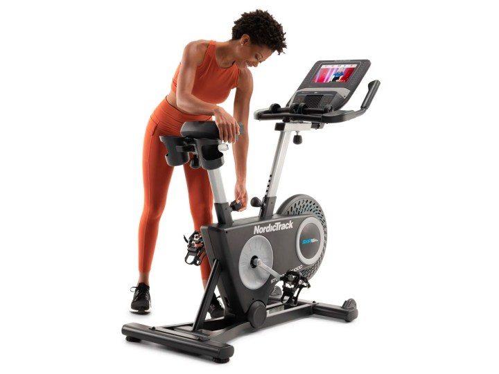 A woman adjusting the NordicTrack Studio Bike 1000 exercise bike against a white background.