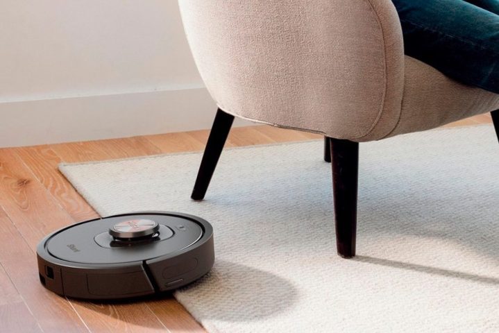 The Shark Matrix robot vacuum cleaning a rug while a person reads in a chair.