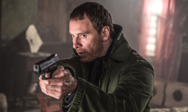 Michael Fassbender as The Killer aiming a gun at something off-camera in The Killer.