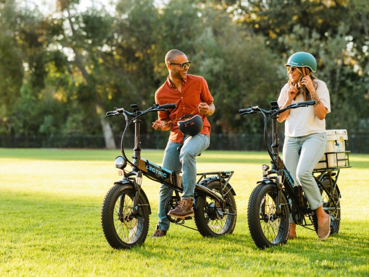 Two people putting on helmets getting ready to ride Lectric XP 3.0 folding e-bikes.