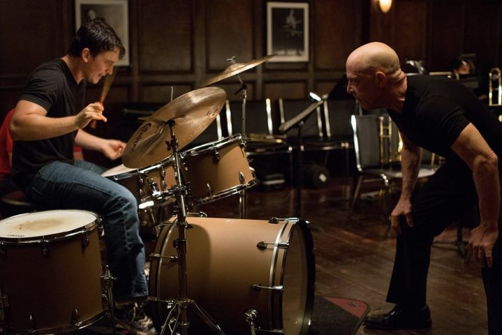 Miles Teller drums while JK Simmons stares in front in Whiplash.