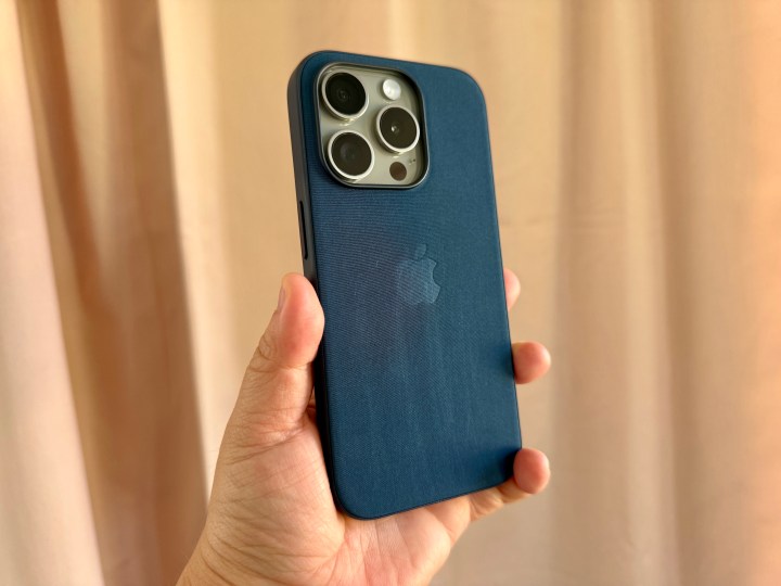 Natural Titanium iPhone 15 Pro in Pacific Blue FineWoven case held in hand showing wear and tear.