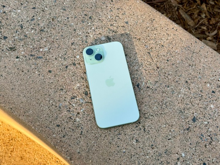 Green iPhone 15 laying flat on a cement bench.