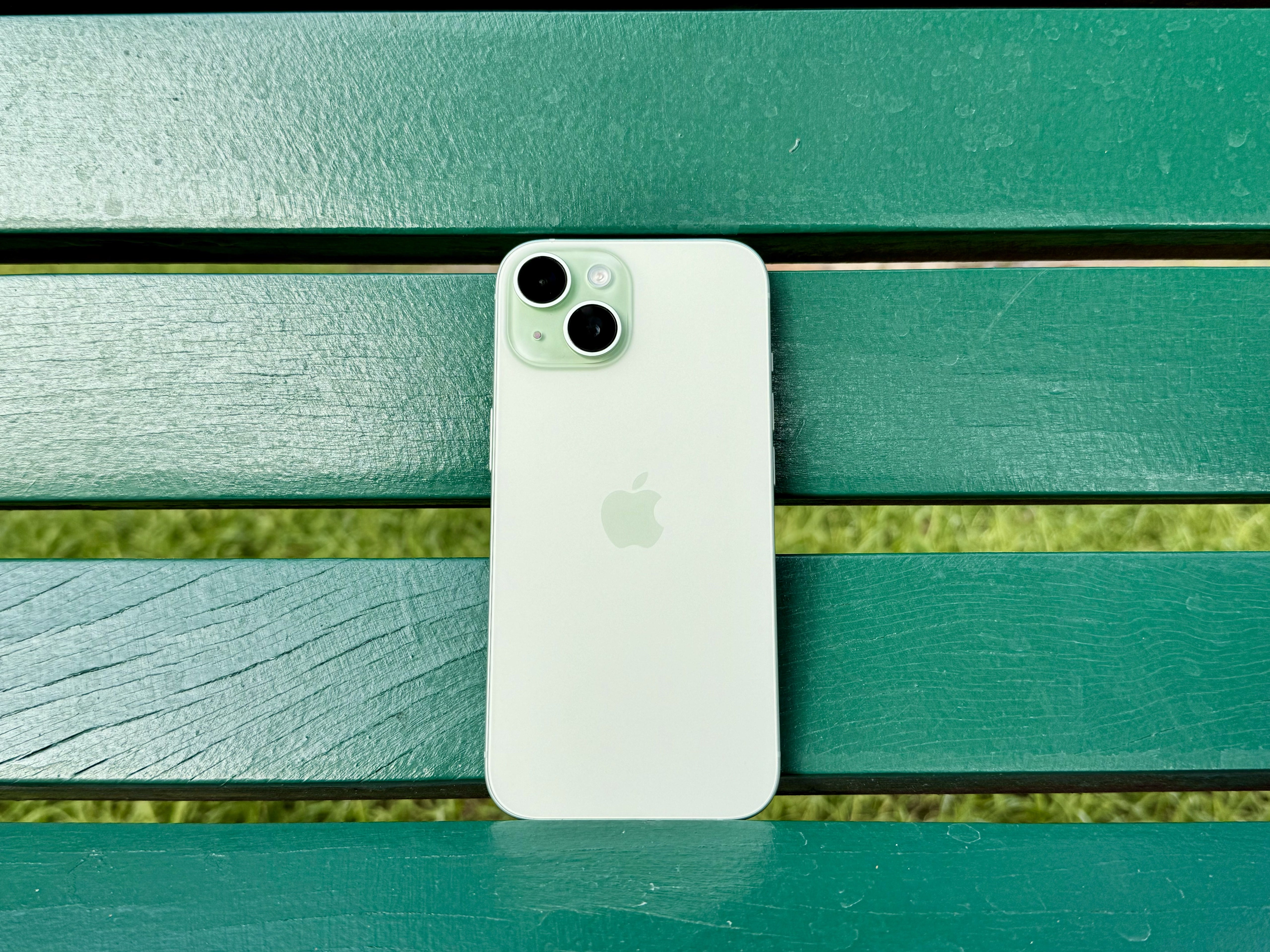 Un iPhone 15 verde sobre un banco verde.