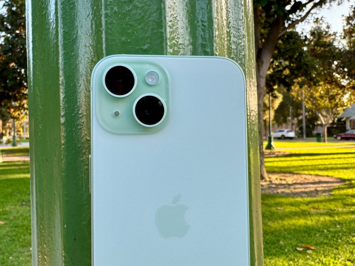 Un iPhone 15 verde apoyado en un poste de luz.