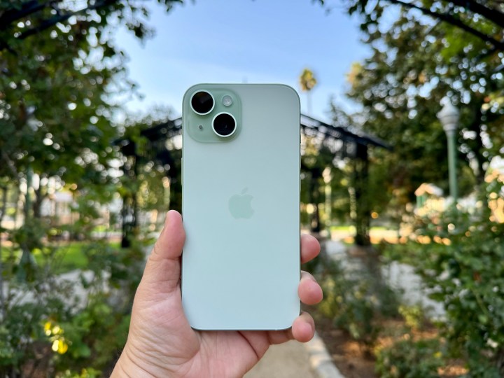 Holding a green iPhone 15 in a rose garden.