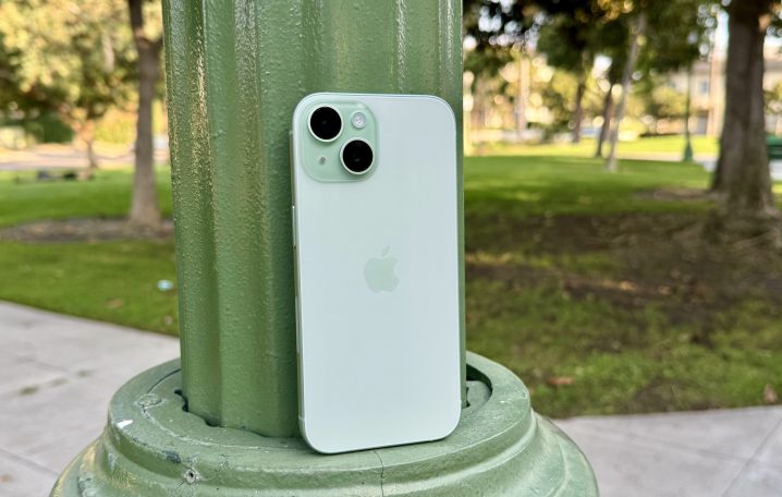 एक हरे रंग का iPhone 15 लैंप पोस्ट पर झुका हुआ है।