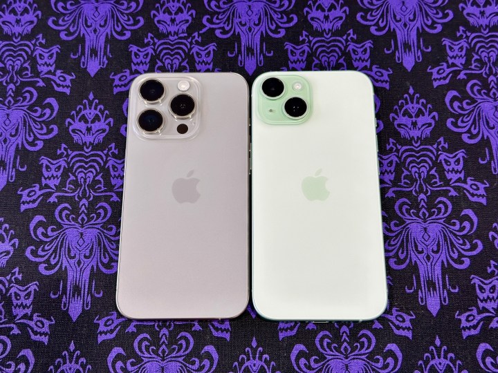 একটি প্রাকৃতিক টাইটানিয়াম আইফোন 15 প্রো (বামে) এবং একটি ভূতুড়ে ম্যানশন ওয়ালপেপার প্লেসমেটে একটি সবুজ iPhone 15।