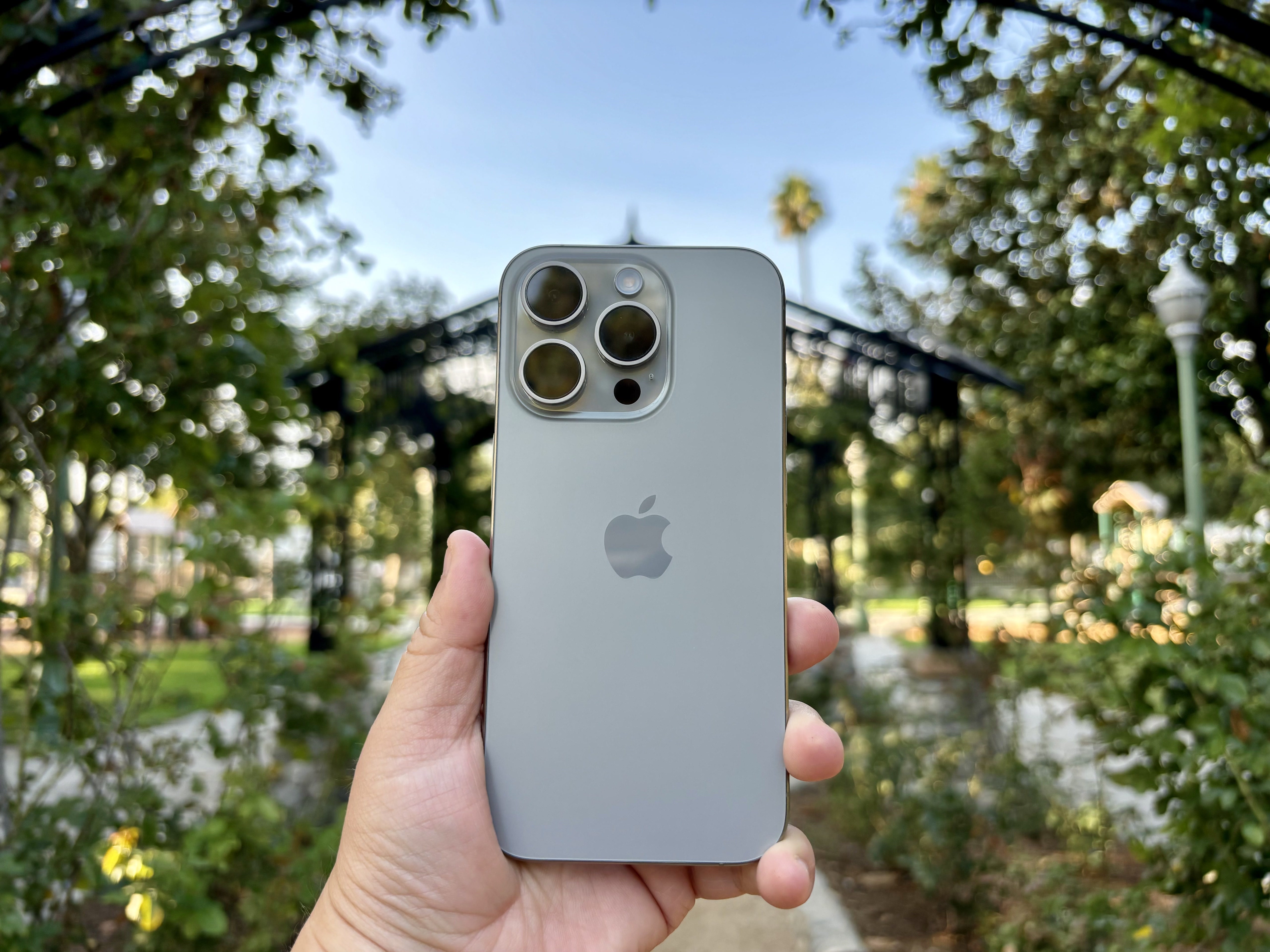 iPhone 15 Pro in Natural Titanium held in hand in rose garden archway.
