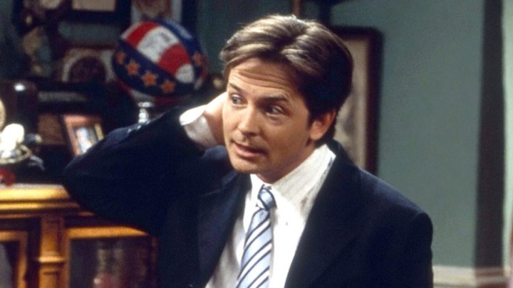 Michael J. Fox with his hand behind his head in a scene from Spin City.