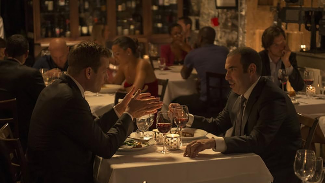 Harvey y Louis sentados en un restaurante hablando en un episodio de Suits.