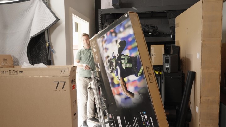 A man navigates a boxed TV into a storage space using a hand truck. 