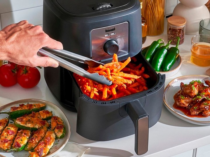 A person removes fries from the basket of the Bella Pro Series 4.2-quart air fryer.