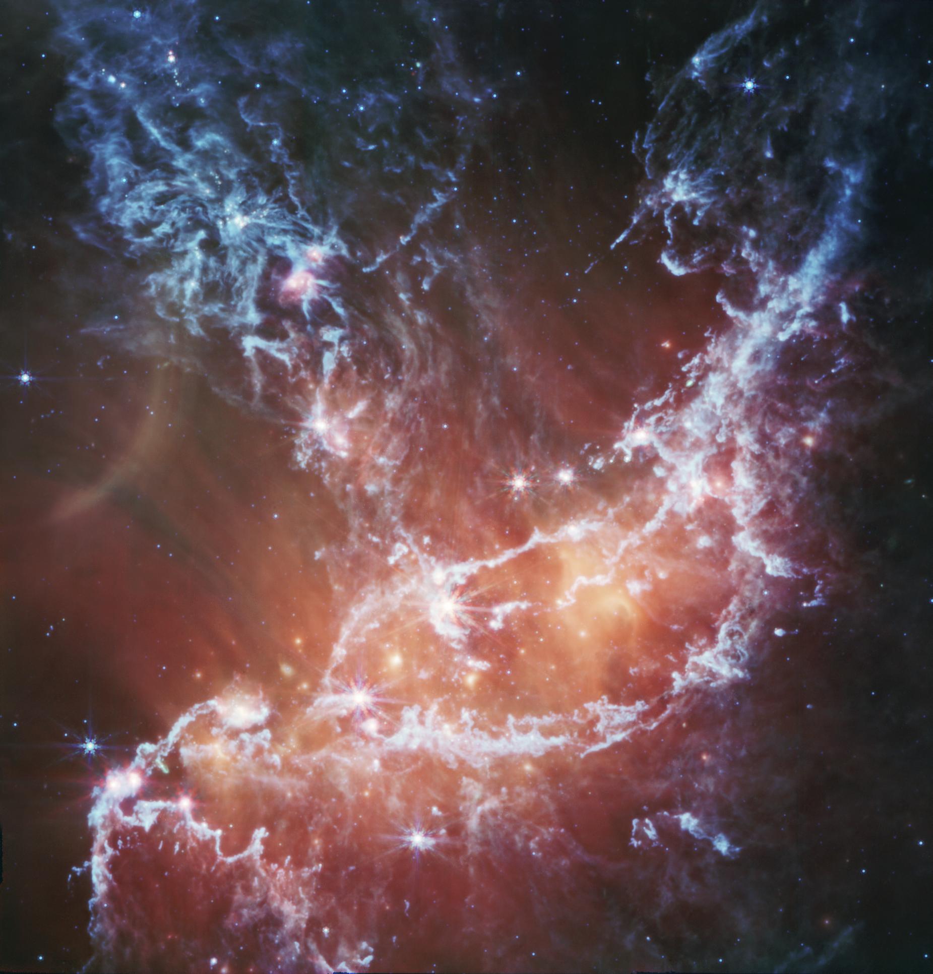 Esta nueva imagen infrarroja de NGC 346 del Instrumento de Infrarrojo Medio (MIRI) del Telescopio Espacial James Webb de la NASA rastrea la emisión de gas frío y polvo. En esta imagen, el azul representa silicatos y moléculas químicas de hollín conocidas como hidrocarburos aromáticos policíclicos o HAP. Una emisión roja más difusa brilla desde el polvo caliente calentado por las estrellas más brillantes y masivas en el corazón de la región. Parches y filamentos brillantes marcan áreas con abundante número de protoestrellas. Esta imagen incluye una luz de 7,7 micras que se muestra en azul, 10 micras en cian, 11,3 micras en verde, 15 micras en amarillo y 21 micras en rojo (filtros de 770 W, 1000 W, 1130 W, 1500 W y 2100 W, respectivamente).