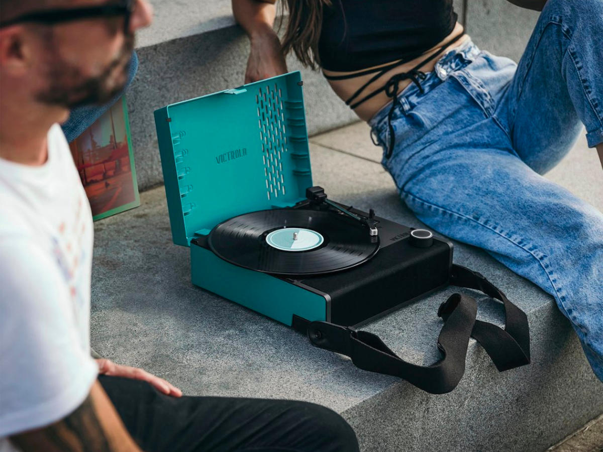 People listen to the Victrola Revolution Go portable record player on the front steps of their home.