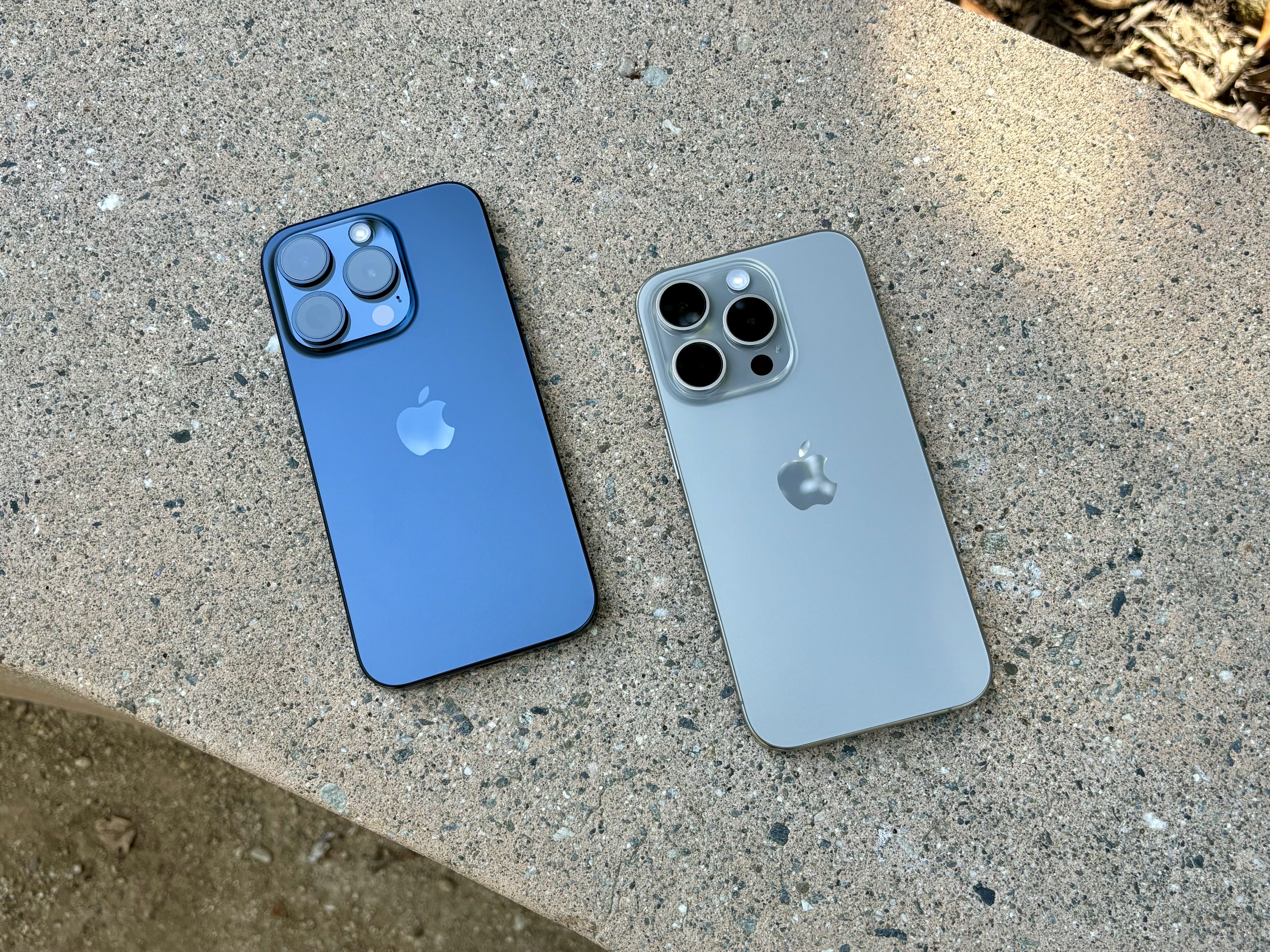 Синий титан (слева) и натуральный титан iPhone 15 плюсов на бетонной скамейке.