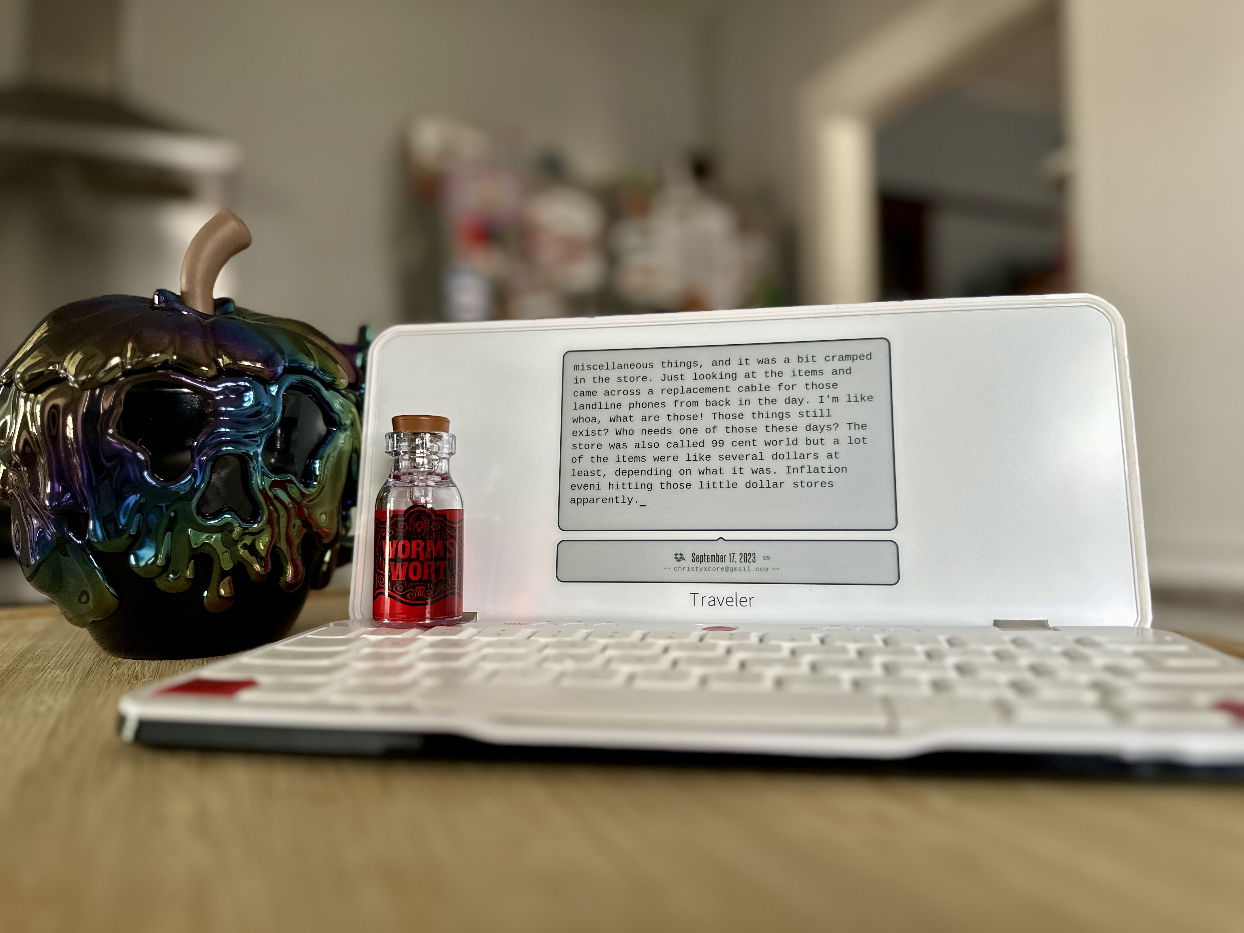 Freewrite Traveler on a table open with a poison apple mug and worm's wort bottle.