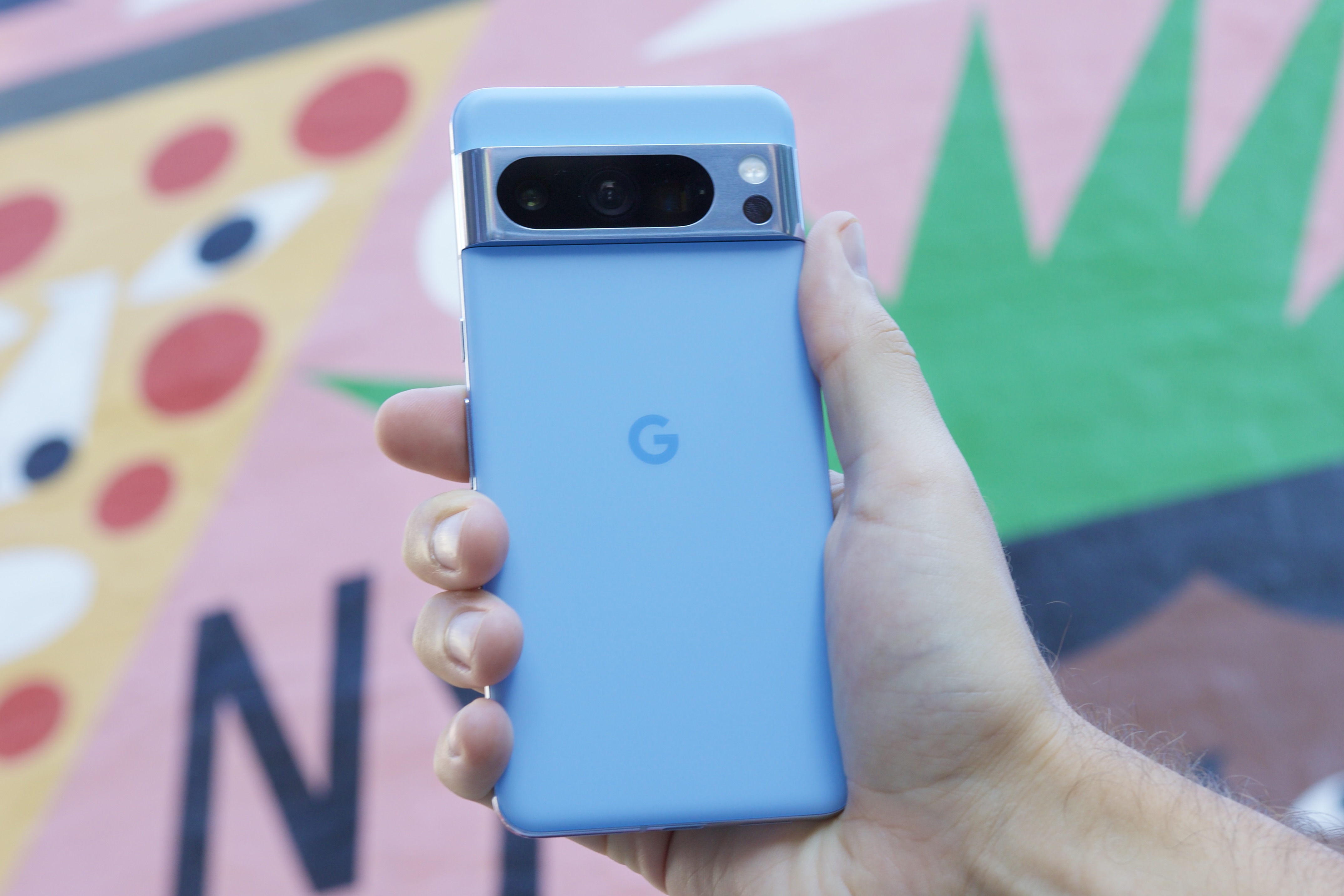 Someone holding the Google Pixel 8 Pro in front of a colorful background.