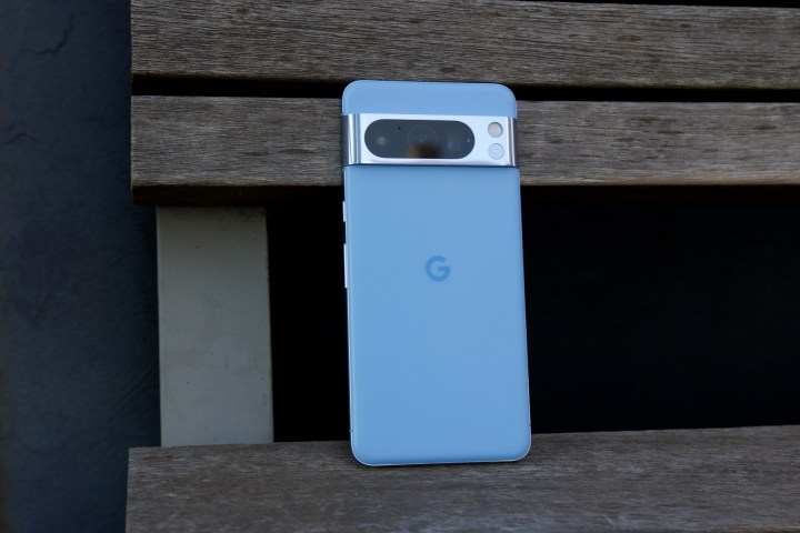 Google Pixel 8 Pro стоит вертикально на скамейке в парке.