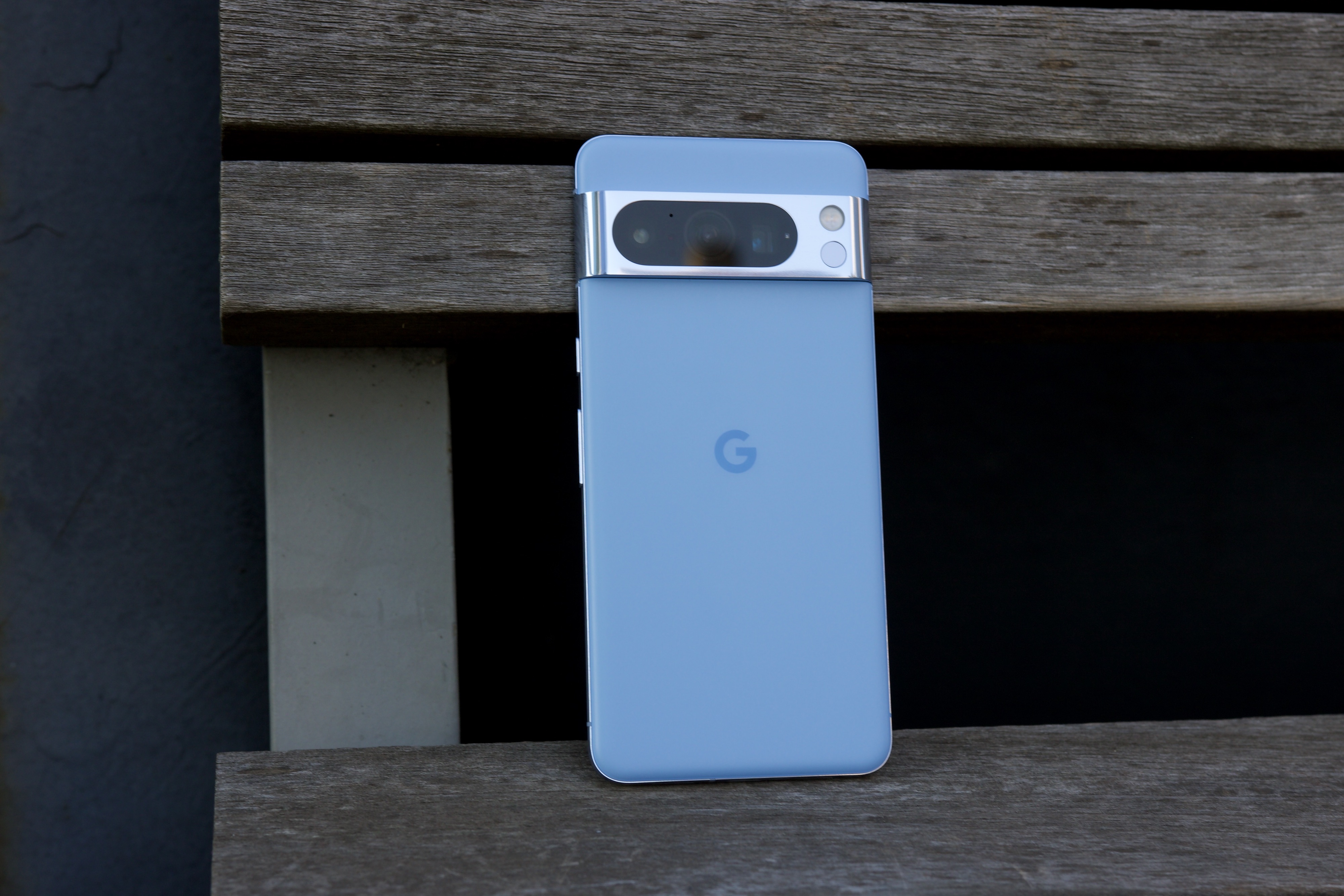 Google Pixel 8 Pro به صورت عمودی روی نیمکت پارک نشسته است.