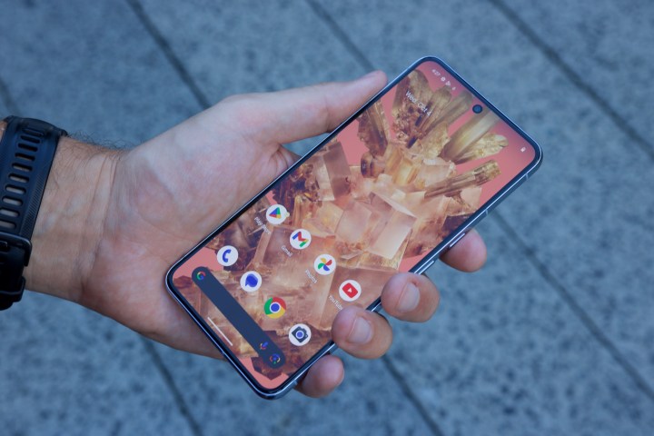 Holding the Google Pixel 8 Pro, showing its Home Screen.