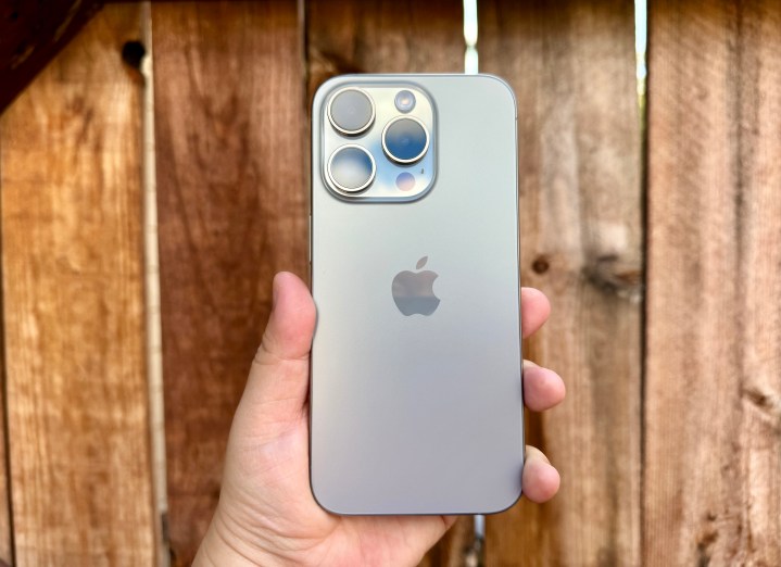 iPhone 15 Pro en titanio natural sostenido en la mano frente a una puerta de madera.