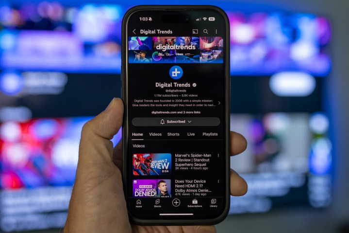The Digital Trends YouTube channel as seen on an iPhone and on a TV in the background.