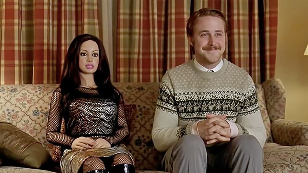 Ryan Gosling como Lars sentado en un sofá junto a una muñeca realista de una mujer en Lars and the Real Girl.