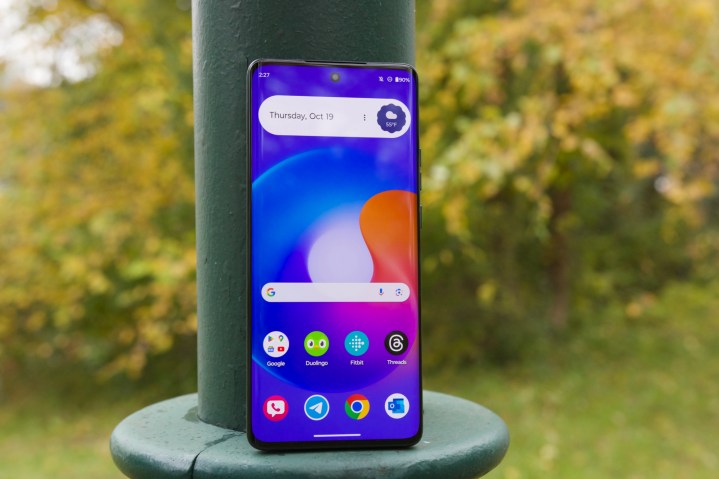 The Motorola Edge (2023) standing against a light pole, with its screen turned on.